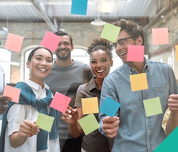 a group of coworkers placing sticky notes onto a glass divider and smiling