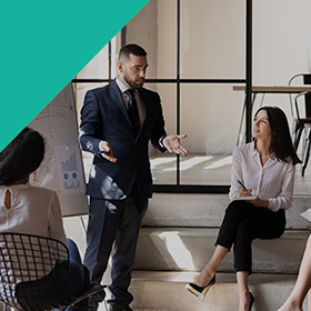 a business man talking with a group of people in an office in front of a whiteboard