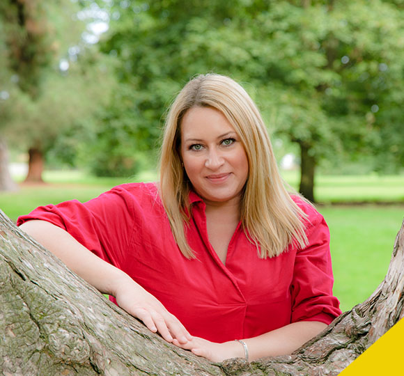 a profile picture of Nathalie McAree behind a tree in a natural scene